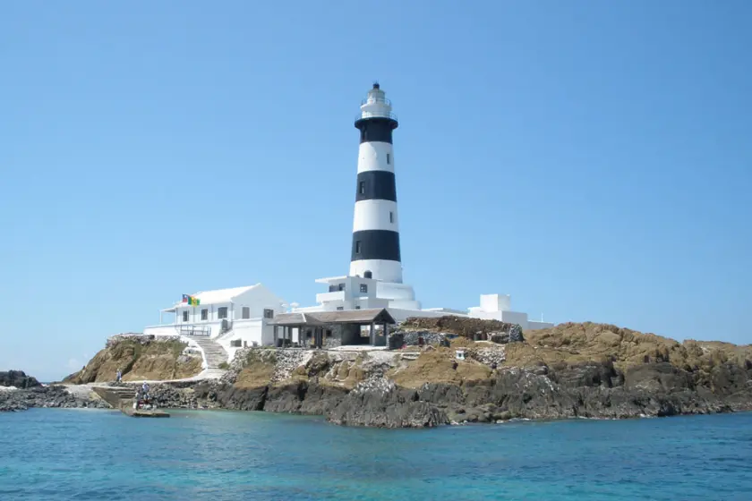 白色與黑色條紋的目斗嶼塔燈矗立於岩石島上，周圍是藍色海水，天空晴朗，氣氛寧靜。