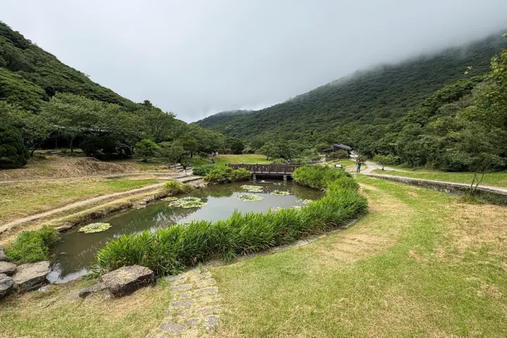 二子坪遊憩區，綠色草地圍繞著一塊小池子，與身後山景