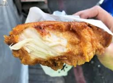 手持一塊裹著紙的炸雞排，雞排外殼金黃酥脆，內部白色嫩滑，顯現熱騰騰的美味。