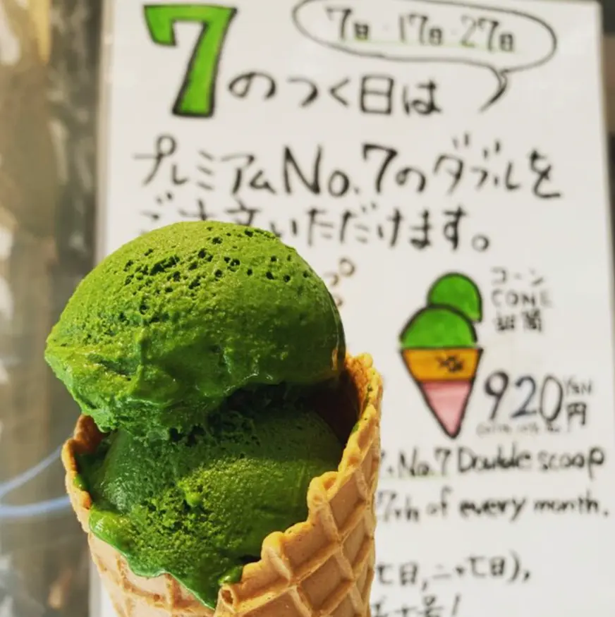 綠色冰淇淋雙球在蛋筒內，背景有標牌，上書有「7」和價格資訊的日文與英文，整體清新又誘人。