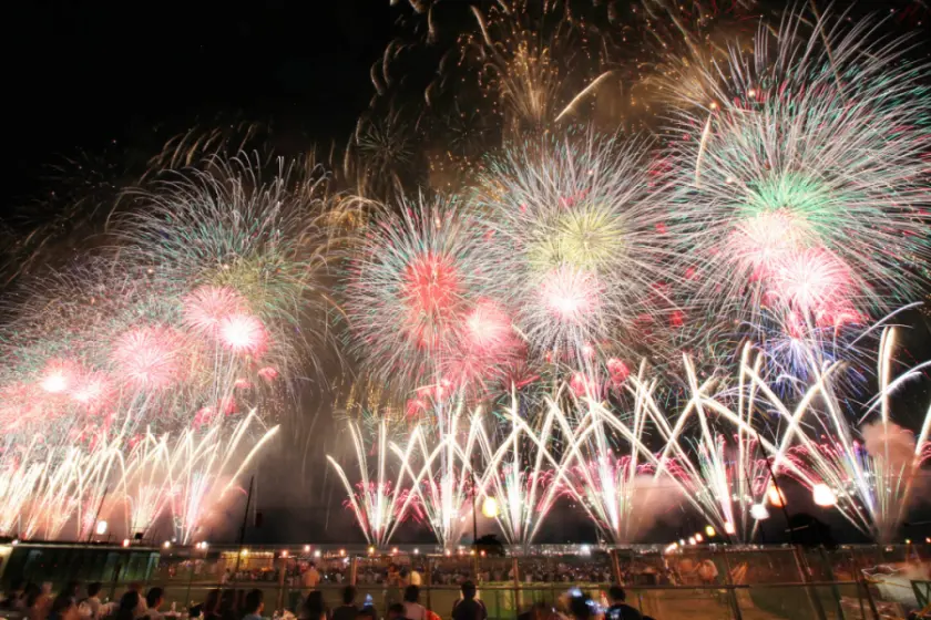 長岡祭花火夜空中絢麗多彩的煙火盛開，底下是觀眾們正在觀看，背景是一片漆黑的天空，氣氛歡快熱烈。