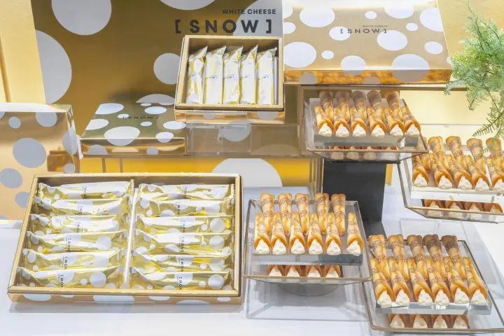 許多透明盒子展示著WHITE CHEESE SNOW餅乾，包裝以金黃色搭配白色點點

