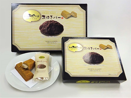 兩個仙台人氣甜點「Saichi 牡丹餅巧克力棒」禮盒，旁邊放有切開的展示巧克力棒在白色盤子上