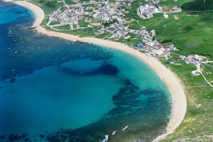 俯瞰網垵口沙灘，碧藍海水與金色沙灘交界，周圍是綠樹成蔭的房屋排列緊密，小鎮寧靜祥和。