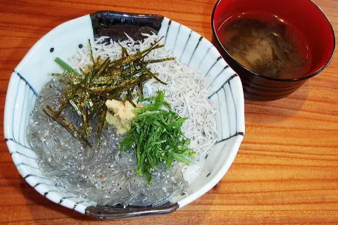 鎌倉必吃美食「生吻仔魚丼」，白色瓷碗中鋪著滿滿的生吻仔魚和青蔥海苔等配料，旁邊附有一五碗味噌湯