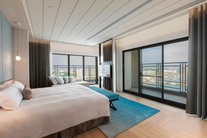 澎澄飯店，寬敞明亮的臥室，設有大床、藍色地毯和窗外城市景觀，氛圍舒適寧靜。