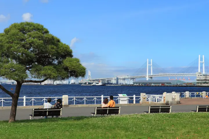 橫濱山下公園海濱步道，遊客坐在長椅上眺望橫濱海灣大橋與湛藍海景