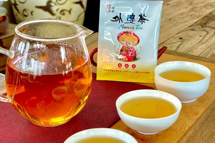 透明茶壺和三杯茶放在木桌上，背景有红色茶袋，上面寫著外婆茶