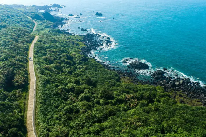  富貴角燈塔步道空拍，步道兩側滿是翠綠植被，緊鄰湛藍北海岸