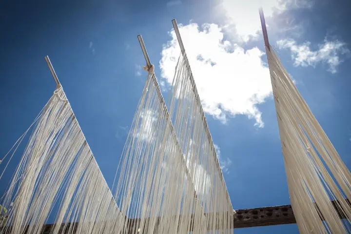 藍色的天空上有稀疏的雲朵，鐵桿子上懸掛著白色細長的麵線