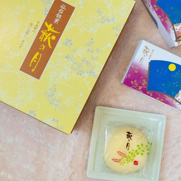 仙台必買伴手禮「萩之月」禮盒，米黃色的禮盒旁展示了一塊黃色高點的樣貌