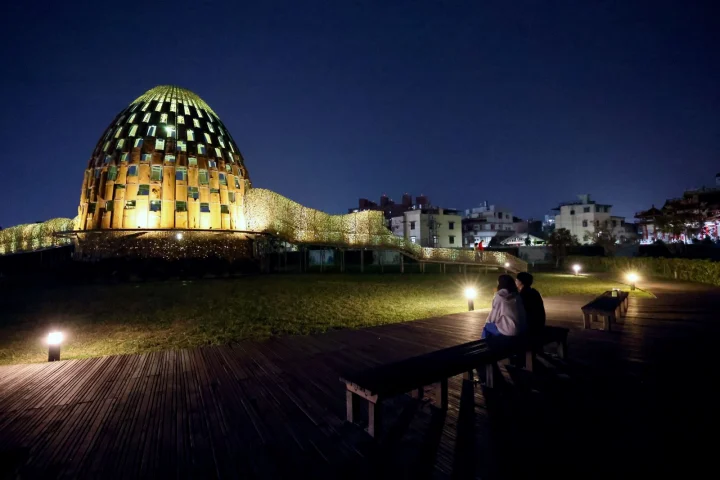 夜晚的嘉義森林之歌，透過光影打光旁邊有兩位遊客坐在椅子上欣賞