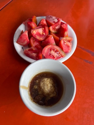 紅色桌面上的白盤子擺放著滿滿的切塊番茄，旁邊搭配著一個碗裝的醬油薑末沾醬