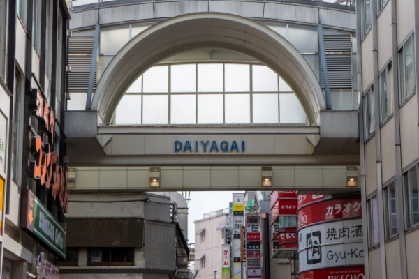 商店街入口上方写有“DAIYAGAI”，两侧有建筑物，背景是多彩的商店招牌和街道，氛围繁忙活跃。
