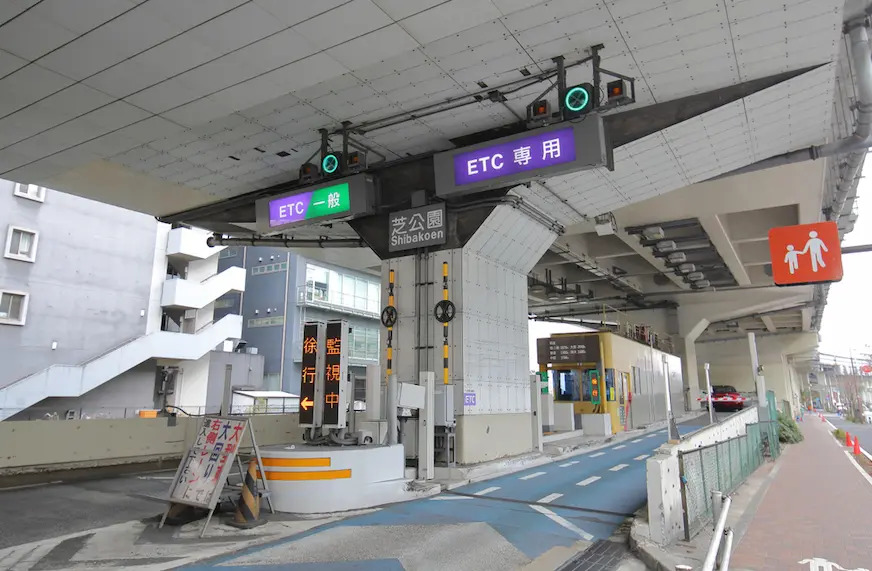 高架下的日本收費站入口，標示「ETC一般」「ETC專用」與「芝公園 Shibakoen」，空蕩安靜，藍白車道明亮。