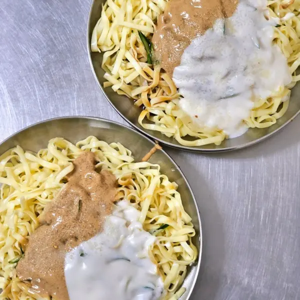 不鏽鋼桌上擺著兩碗美乃滋和麻醬的涼麵