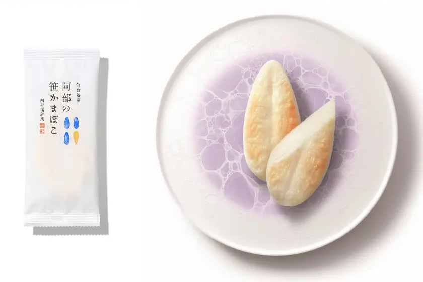 仙台名產「阿部蒲鉾店」竹葉魚板，放在白色盤子上的兩片魚板，表面微黄色。左側白色包裝上印有藍黃標示