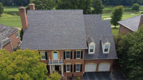 Aerial view of a finished synthetic cedar shake roof on a two-story brick home in Maryland, showing multiple roof planes, dormers, and two chimneys.