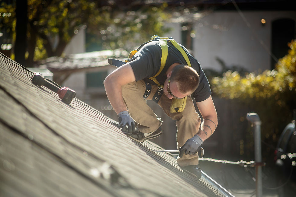Roofing contractor wearing a safety harness, repairing shingles on a sloped residential roof in daylight.