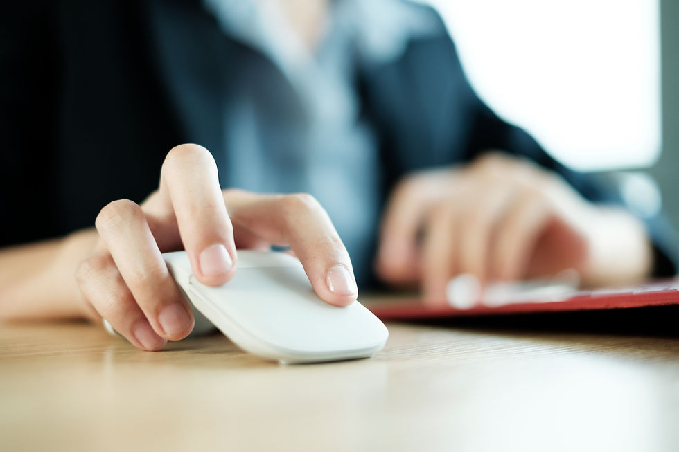 Close-up of a person using a white computer mouse at a desk, with a blurred keyboard and business attire in the background.