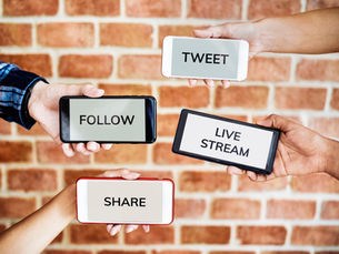 Four hands hold smartphones labeled TWEET, FOLLOW, LIVE STREAM, and SHARE against a brick wall.