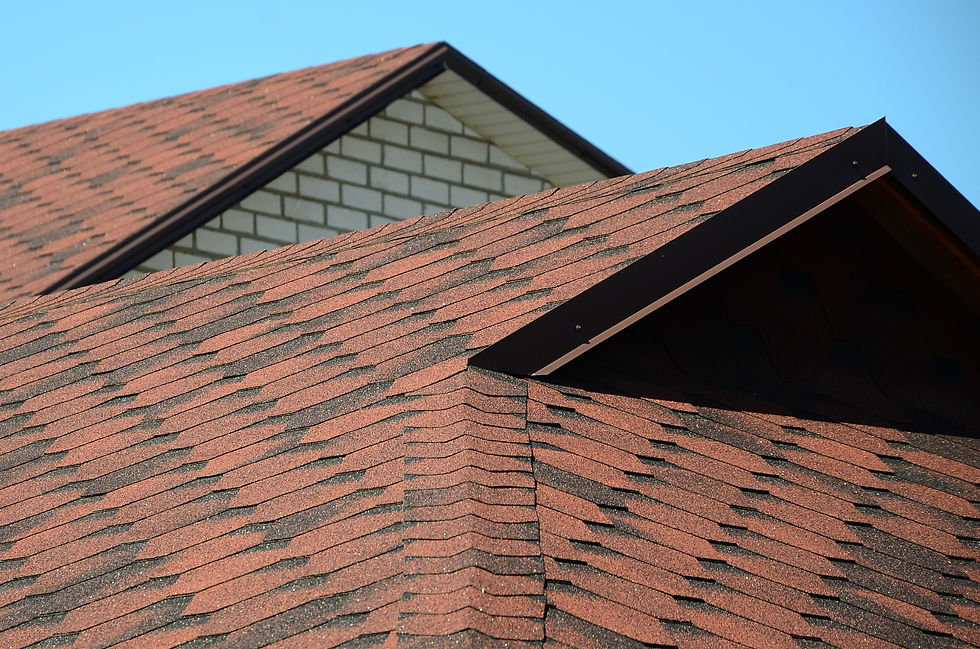 Close-up of red shingled house roofs with a white brick gable against a clear blue sky.
