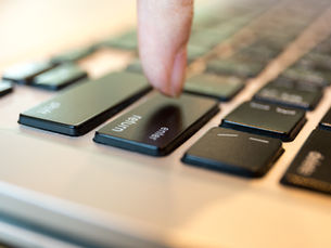 Close-up of a finger pressing the Enter key on a laptop keyboard, with Return visible in soft warm light.