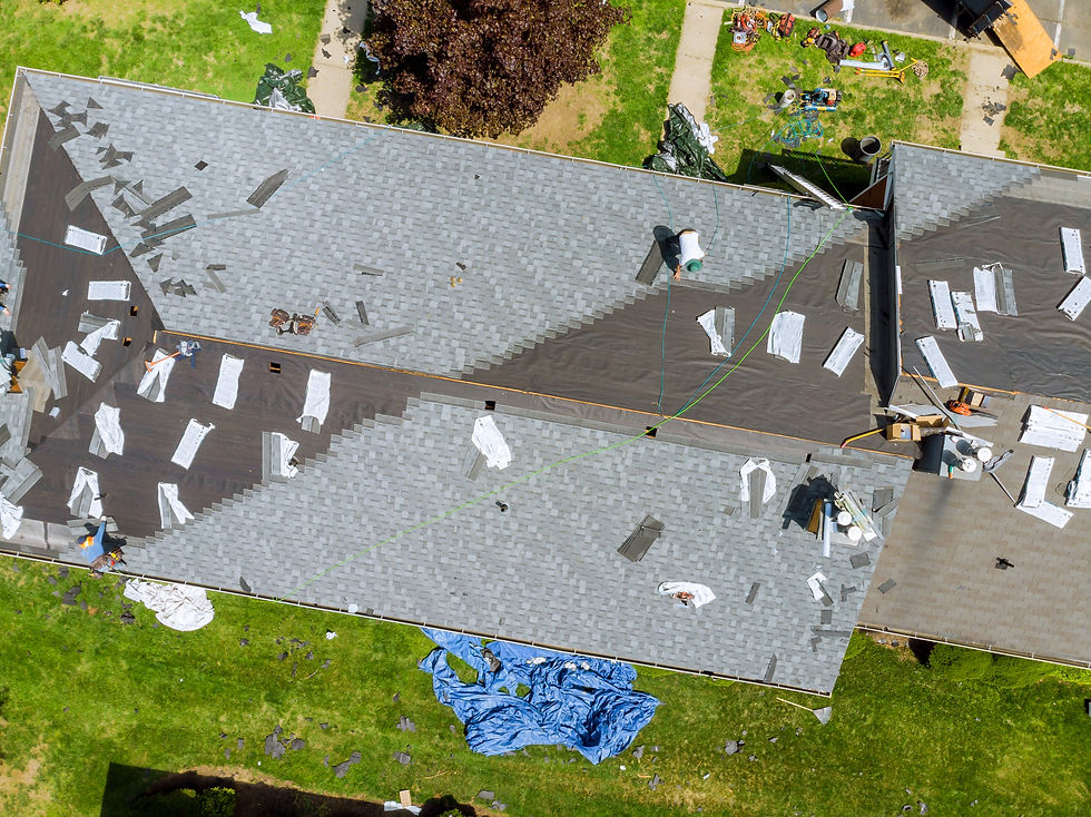 Aerial view of roofers replacing a gray shingle roof, with tools, tarps, and workers on a suburban house.