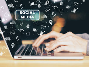 Hands typing on a laptop with "Social Media" text and doodles of clouds, arrows, and envelopes, against a blurred dark background.