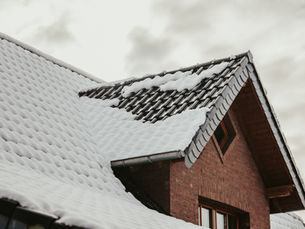 Snow-covered brick house roof with dark tiles under an overcast sky, a quiet winter scene