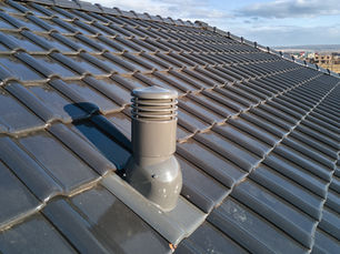Dark gray tiled roof with a vent pipe under a bright sky, showing a clean, newly installed rooftop.