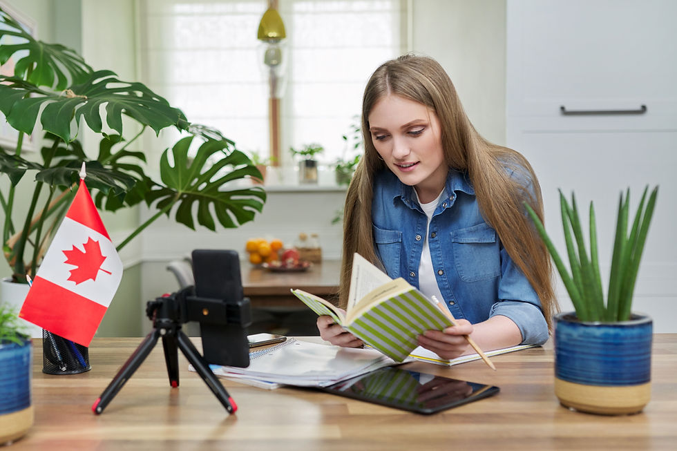 Woman reading a striped notebook at a desk with a small Canadian flag, camera tripod, and houseplants in a bright room.