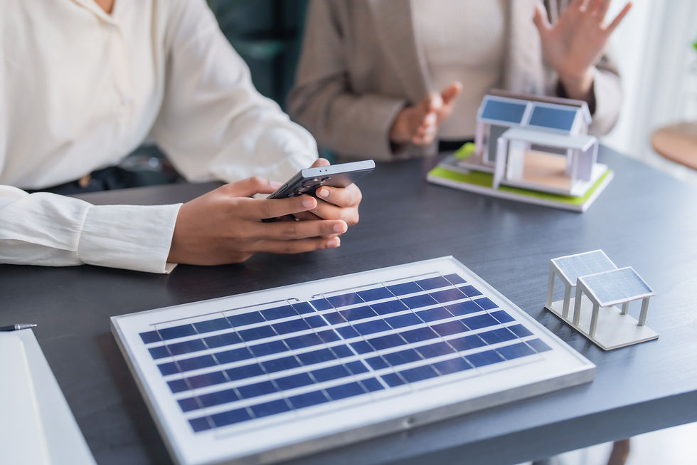 People discuss solar panel models at a table, one using a smartphone, in a bright office, with no visible text.