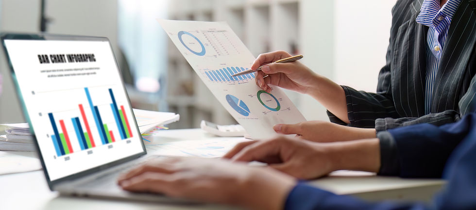 Business meeting with laptop showing BAR CHART INFOGRAPHIC and printed charts; a person points at graphs in a bright office.