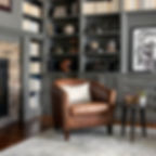 A traditional reading space with a leather armchair, gray shelving with books and decor, and a small round table on a soft rug.