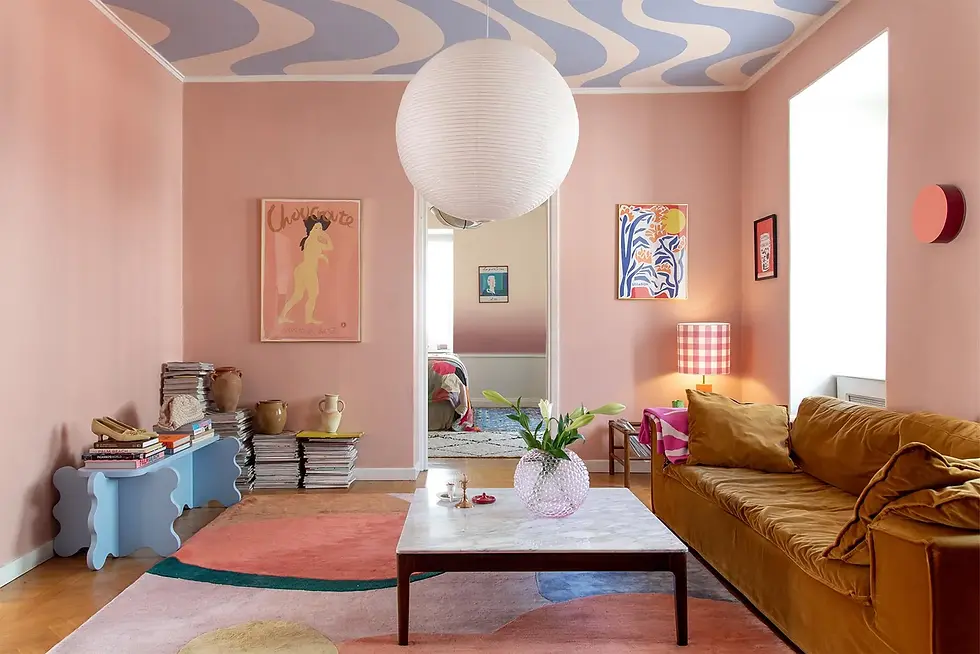 A vibrant retro-style living room with pink walls, wave-patterned ceiling, eclectic furniture, and a multi-colored area rug.