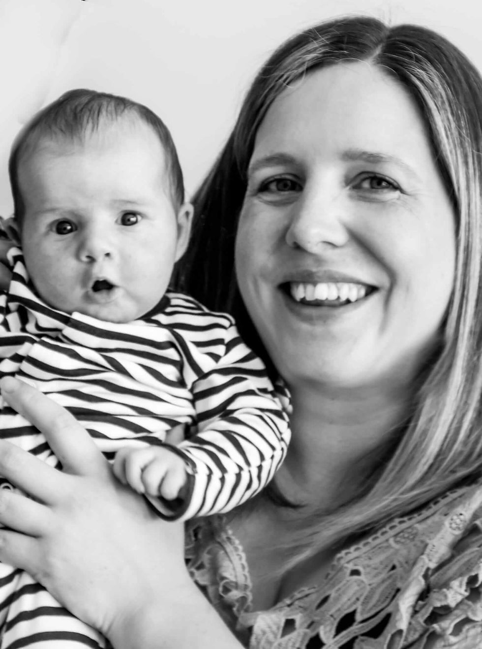 A mum who completed a Positive Birth Leeds Hypnobirthing course holds her baby and is smiling at the camera, baby's mouth is open. The photo is greyscale.