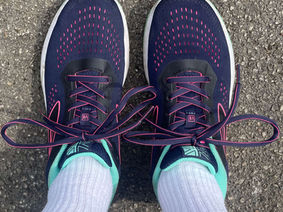 Feet wearing blue trainers on the pavement. The picture is take from above looking down at the shoes. 