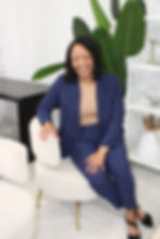 Angelik Holloway Georgia Acquisition Healthcare Compliance Lawyer in a blue suit sits on a cream chair in a bright room with large green leaves, white shelves, and neutral décor.