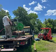 Man operating portable sawmill on truck, tractor in background