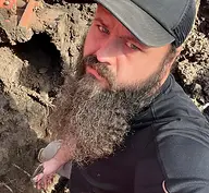 Bearded man in baseball cap standing in a trench