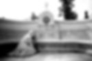 Statue of mourning woman kneels at a Houdini memorial. Bust atop stone bench with engraved "HOUDINI WEISS." Trees and sky in background.