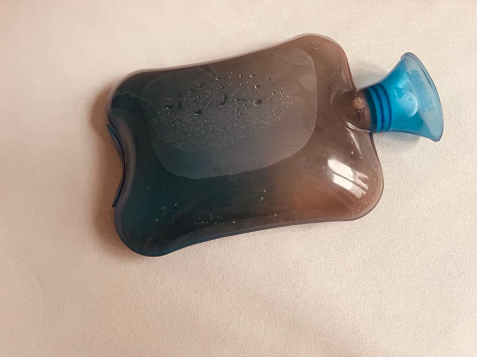 Dunkelbraune Wärmflasche mit blauer Öffnung, teils mit Wassertropfen bedeckt, liegt auf beigefarbenem Hintergrund.