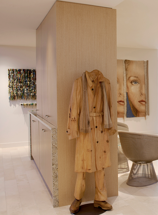 Custom millwork volume in An Artful Existence acting as a screen to divide spaces while maintaining openness, concealing a structural column and integrated bar, and providing a backdrop for sculpture and artwork, by Jaffe Architecture