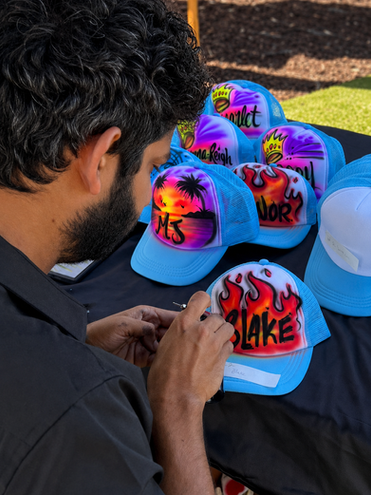 Artist painting custom hats at a live airbrush event.