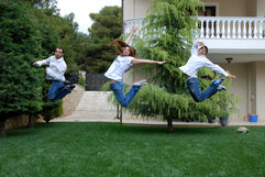 Three people are jumping happily on a green lawn outside a house.