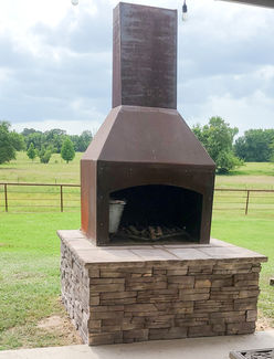 An outdoor metal fireplace is built on a dark brown stone platform.