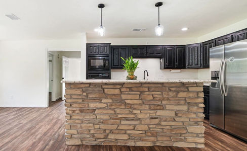 Classy rustic kitchen with black cabinets and mixed brown stone veneer accent island.