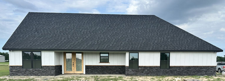Front view of small house with white siding and black drystack stone veneer wainscoting.
