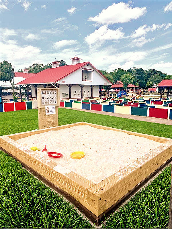 Large wooden sandbox, sand toys, colorful fences, red-roofed building attraction.